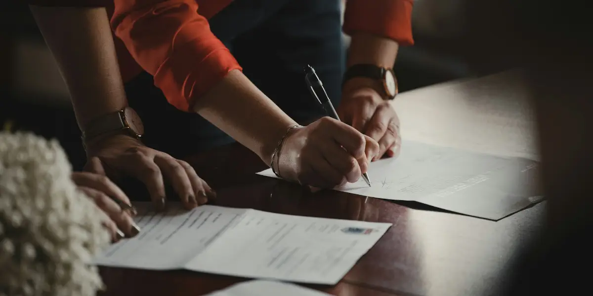 Two people signing a business purchase agreement at a dark wooden table