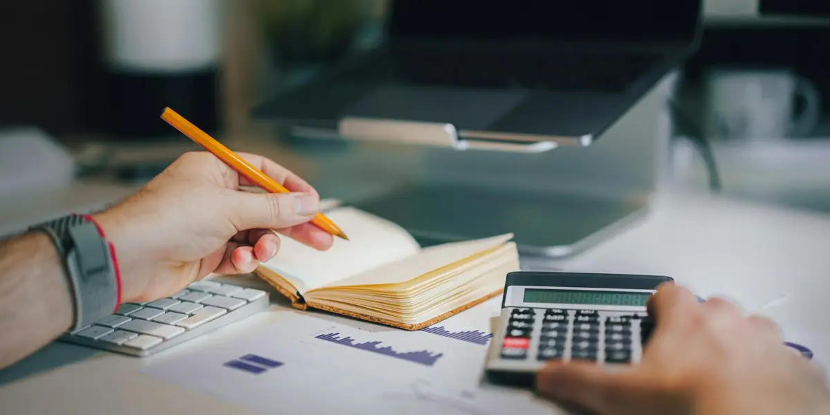 A buyer working through loan payments with a calculator, notebook and laptop