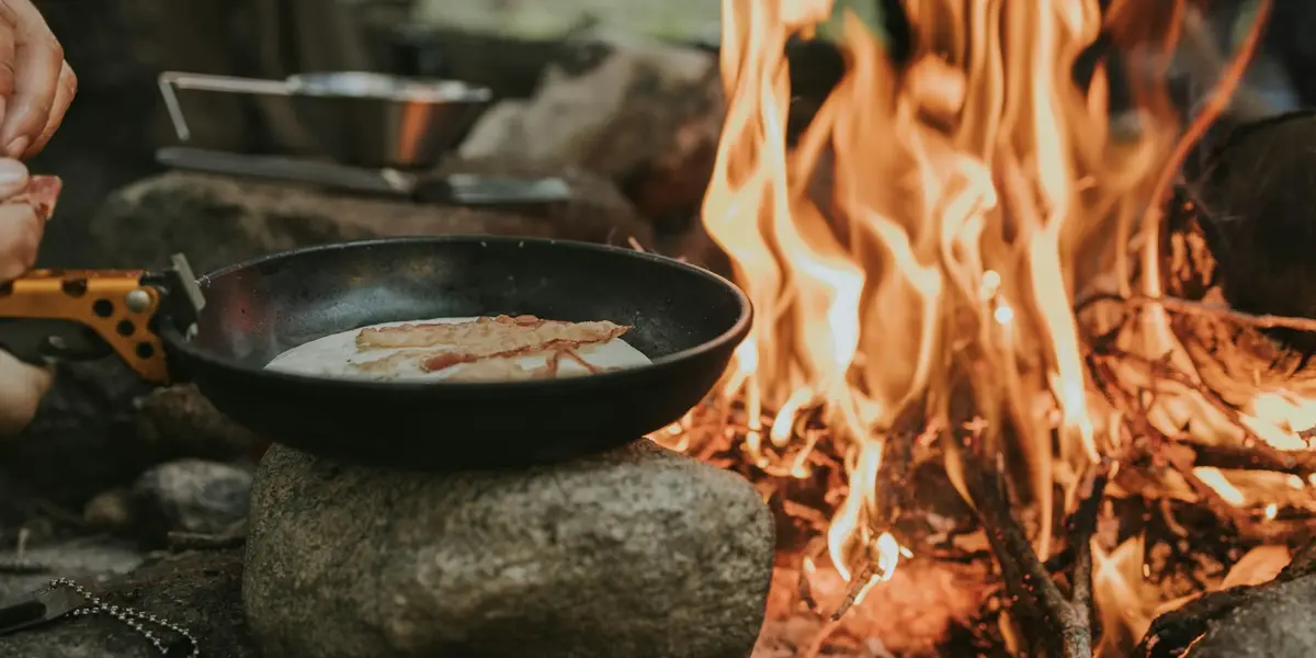 A skillet cooking over a campfire, the kind of scene a camp-cooking review site publishes